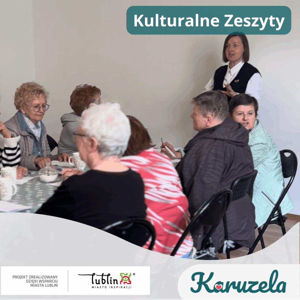 Grupa uczestników, głównie kobiet w wieku senioralnym, siedzi przy stole podczas zajęć ‘Kulturalne Zeszyty’. Przed nimi znajdują się kartki, długopisy i filiżanki. W tle stoi prowadząca w białej koszuli i ciemnym bezrękawniku, mówi do grupy. Na grafice widoczny jest tytuł ‘Kulturalne Zeszyty’ oraz logotypy: Miasta Lublin, projektu ‘Projekt zrealizowany dzięki wsparciu Miasta Lublin’ i fundacji Karuzela